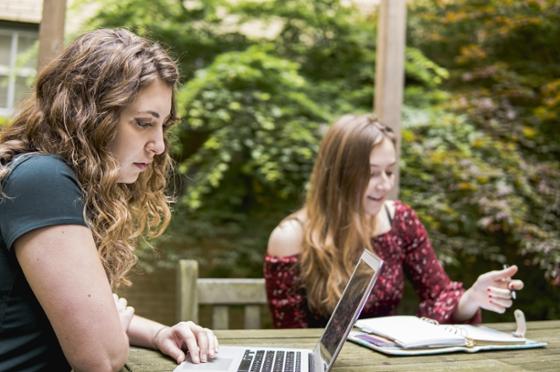 两名足球外围买球靠谱(Chatham University)的学生坐在外面的一张小酒馆桌旁，用笔记本电脑独立学习. 